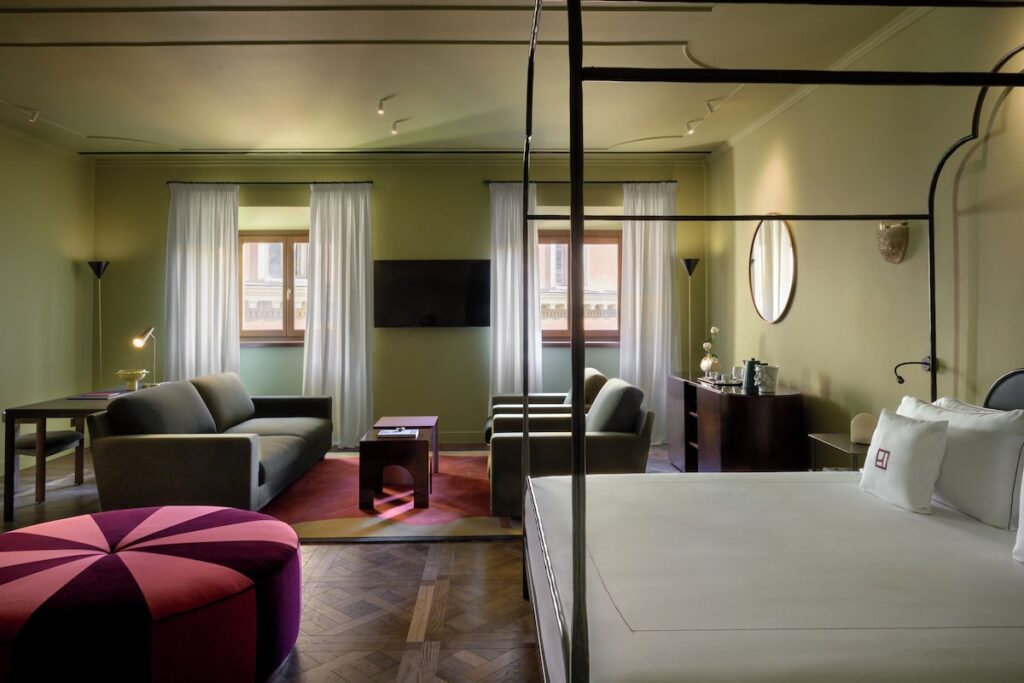 Decoração da Suíte de Luxo no hotel Palazzo Talìa em Roma com cama de dossel de ferro, sofá verde e pufe de veludo rosa.