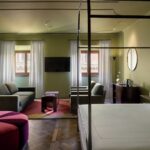 Decora&ccedil;&atilde;o da Su&iacute;te de Luxo no hotel Palazzo Tal&igrave;a em Roma com cama de dossel de ferro, sof&aacute; verde e pufe de veludo rosa.