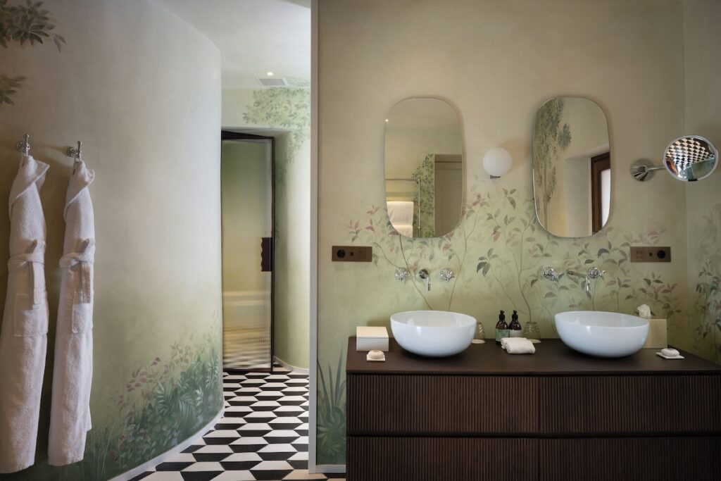 Banheiro duplo na Suíte Premium do hotel Palazzo Talìa com pintura mural botânica, piso geométrico tridimensional e cubas duplas.