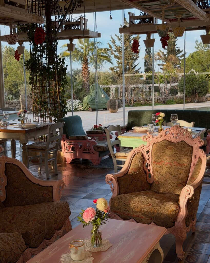 Salão envidraçado com poltronas vintage em tons rosa e verde na Masseria Montenapoleone.