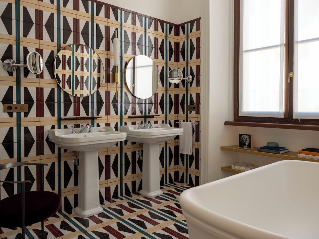 Banheiro da Suíte Jr no Palazzo Talìa revestido com azulejos gráficos geométricos coloridos, lavatórios duplos e banheira vitoriana.