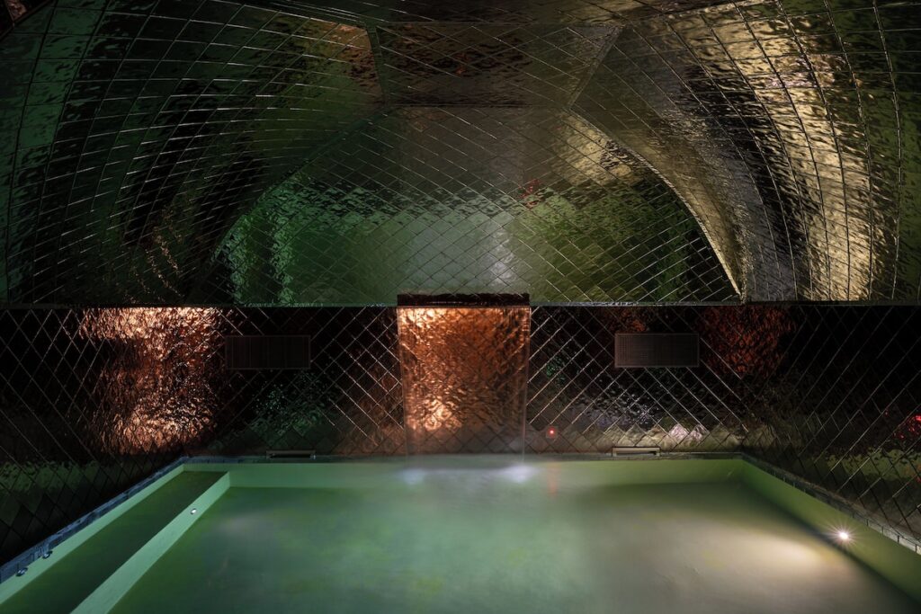 Piscina interna do spa no Palazzo Talìa revestida por placas espelhadas bronze sob teto abobadado com iluminação cênica.