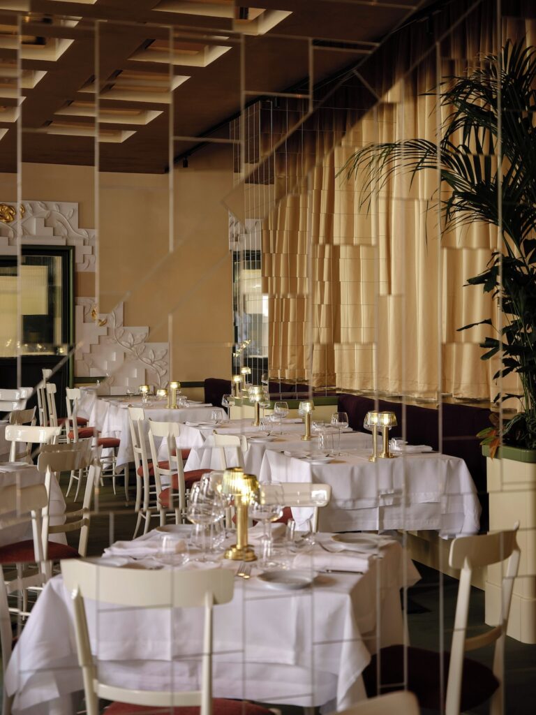 Salão do restaurante no Palazzo Talìa com mesas postas elegantes, iluminação em latão e painel de espelhos facetados.