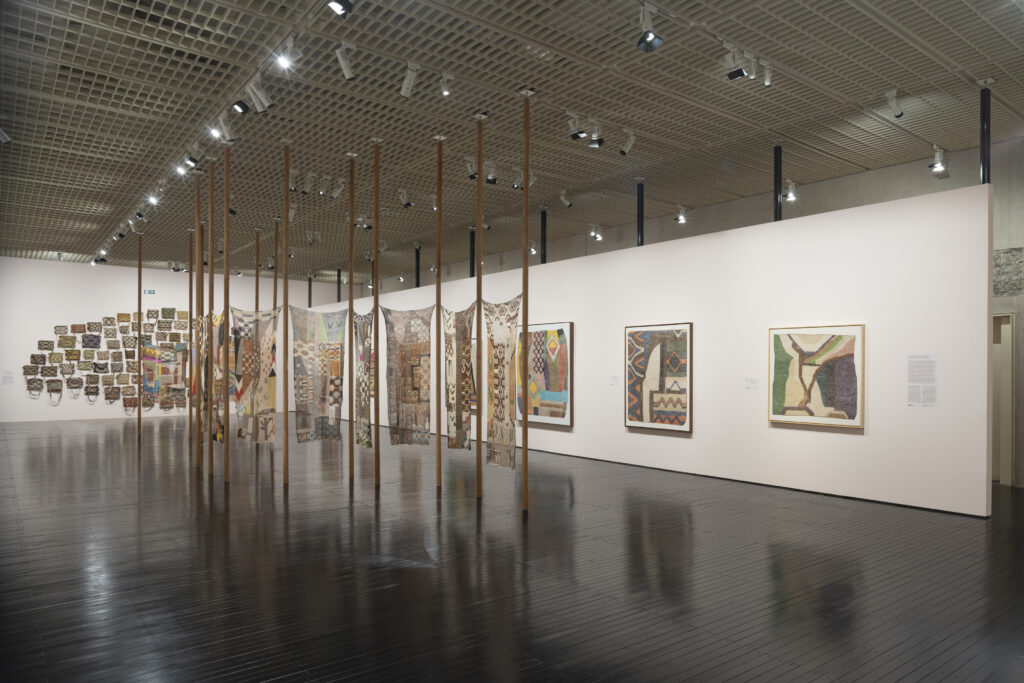 Obras têxteis e bolsas tecidas suspensas em galeria do MASP, em destaque nas exposições em São Paulo focadas em técnicas manuais e biofilia.