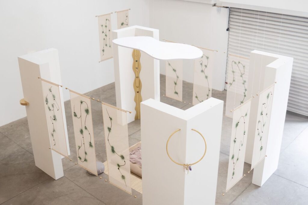 Instalação com colunas brancas, tecidos translúcidos e futon na Galeria Luís Maluf, do roteiro de exposições em São Paulo sobre bem-estar.