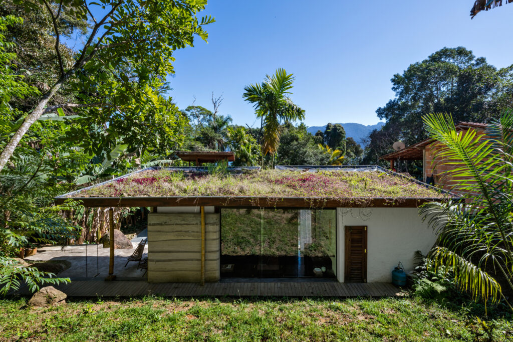Teto verde e paredes de taipa na Casa de hóspedes em Paraty, integrando arquitetura vernacular à Mata Atlântica.