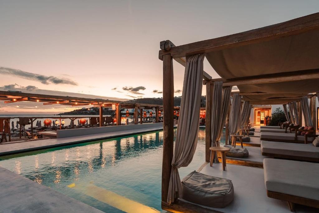 Cabanas de madeira à beira da piscina ao pôr do sol no Branco Mykonos, cenário sofisticado de onde ficar em Mykonos.