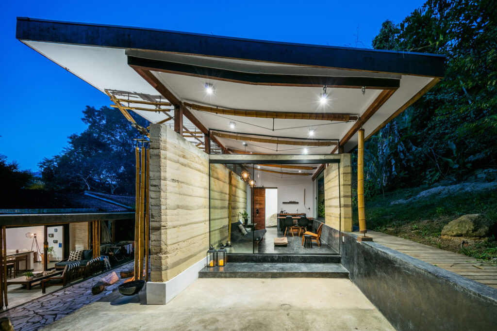 Pavilhão iluminado da Casa de hóspedes em Paraty com cobertura inclinada em bambu e arquitetura vernacular.
