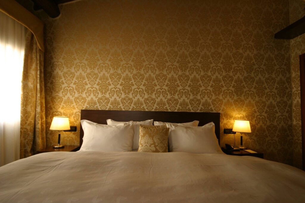 Quarto clássico com papel de parede damasco dourado no Ca Maria Adele, sofisticação nos hotéis de Veneza.