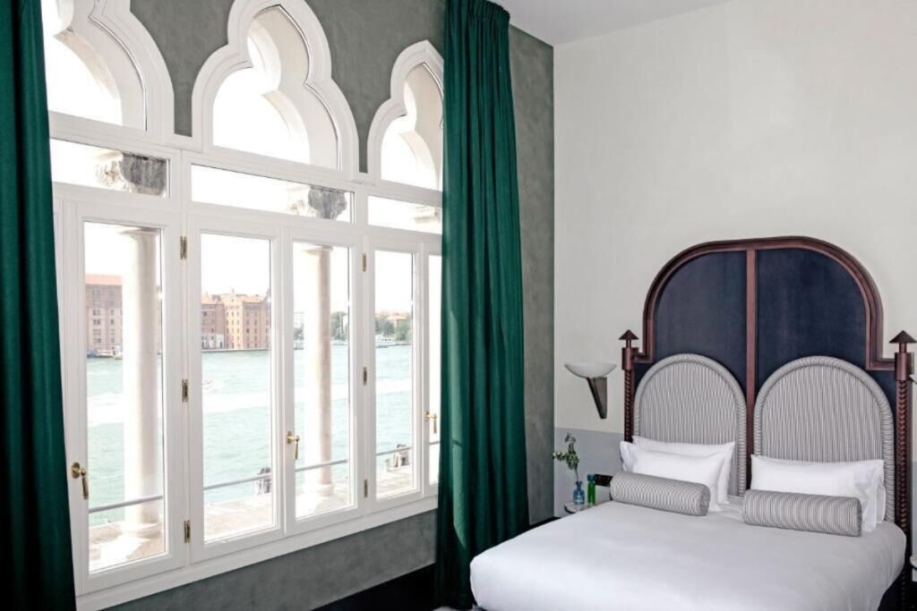Quarto com janelas góticas e vista para o canal no Il Palazzo Experimental, inovação nos hotéis de Veneza.