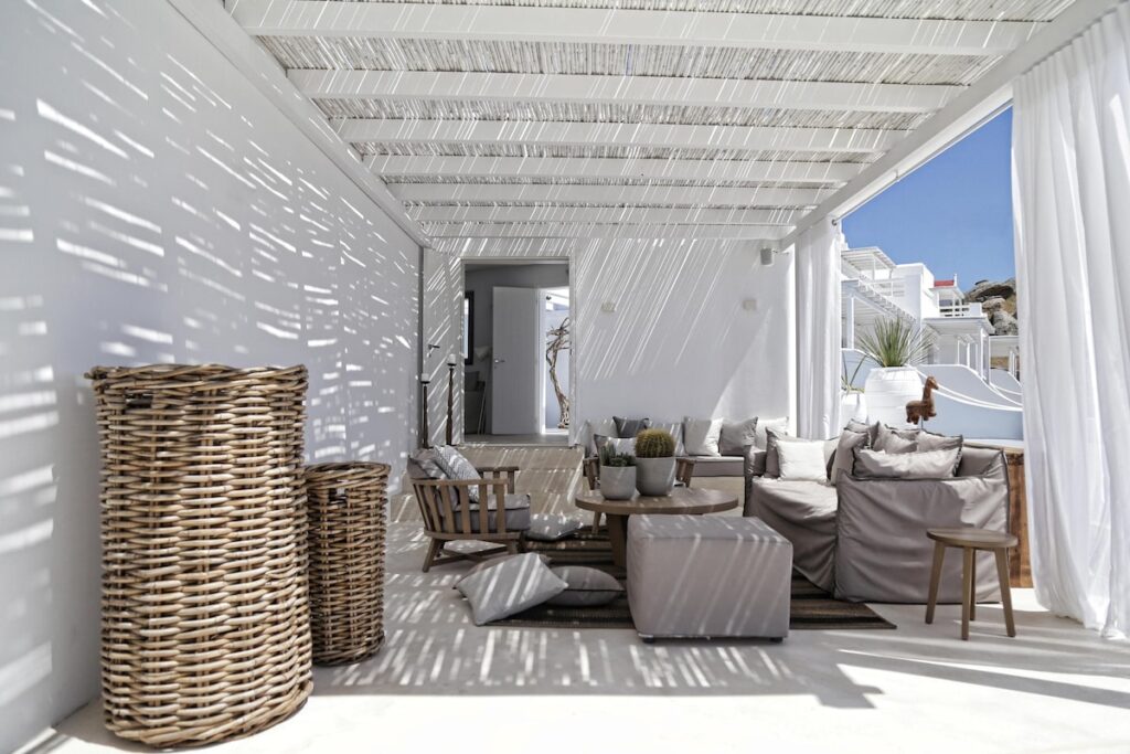 Terraço sombreado por pérgula com mobiliário em fibra natural no Livin Mykonos Hotel, charme de onde ficar em Mykonos.