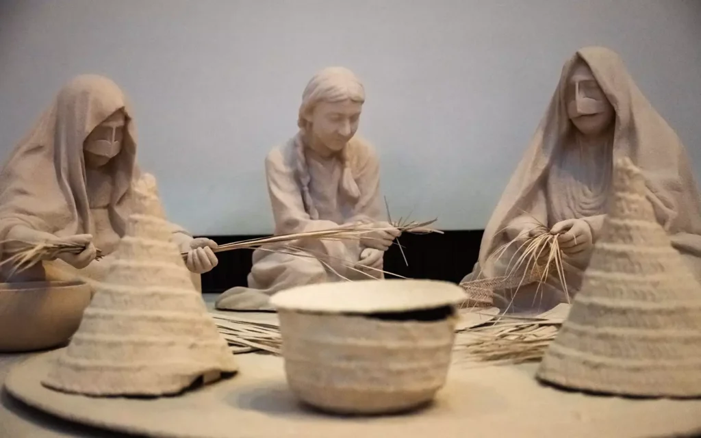 Diorama escultórico no Zayed National Museum representando mulheres em trajes tradicionais tecendo palha de tamareira.