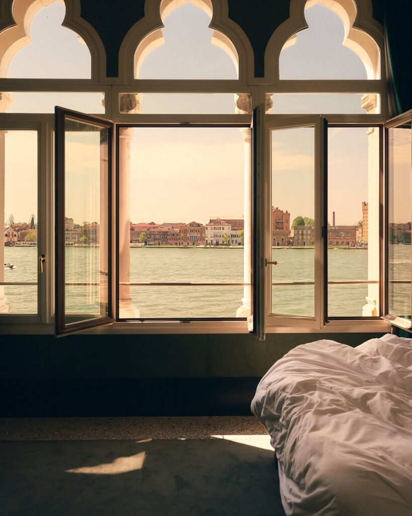 Vista da cama para o canal através de janelas góticas no Il Palazzo Experimental, poética dos hotéis de Veneza.