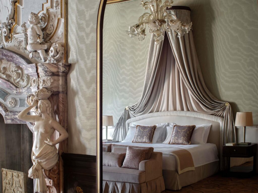 Detalhe da lareira em mármore esculpido e cama com dossel no Orient Express Venezia, requinte dos hotéis de Veneza.