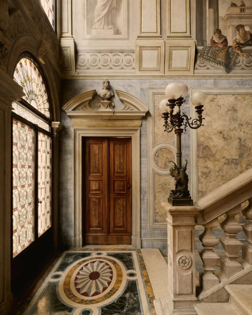 Escadaria monumental com afrescos e piso em mármore no Palazzo Papadopoli do Aman Venice, tradição dos hotéis de Veneza.
