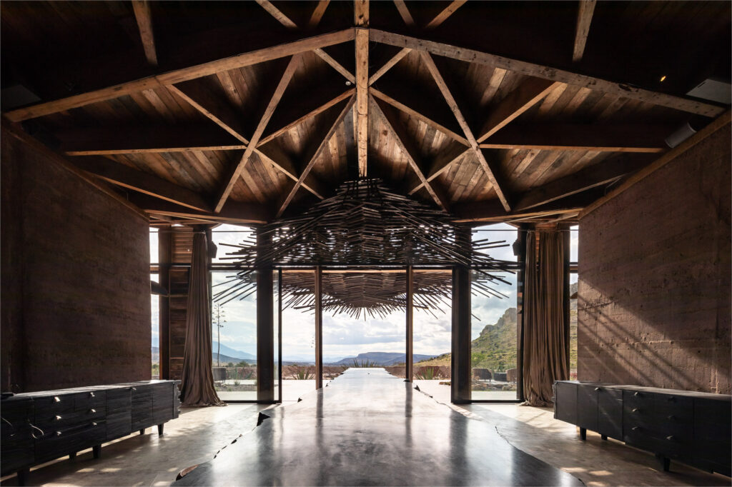 Mesa comunal monumental e estrutura em madeira na Casa Silencio, unindo design de interiores e arquitetura vernacular.