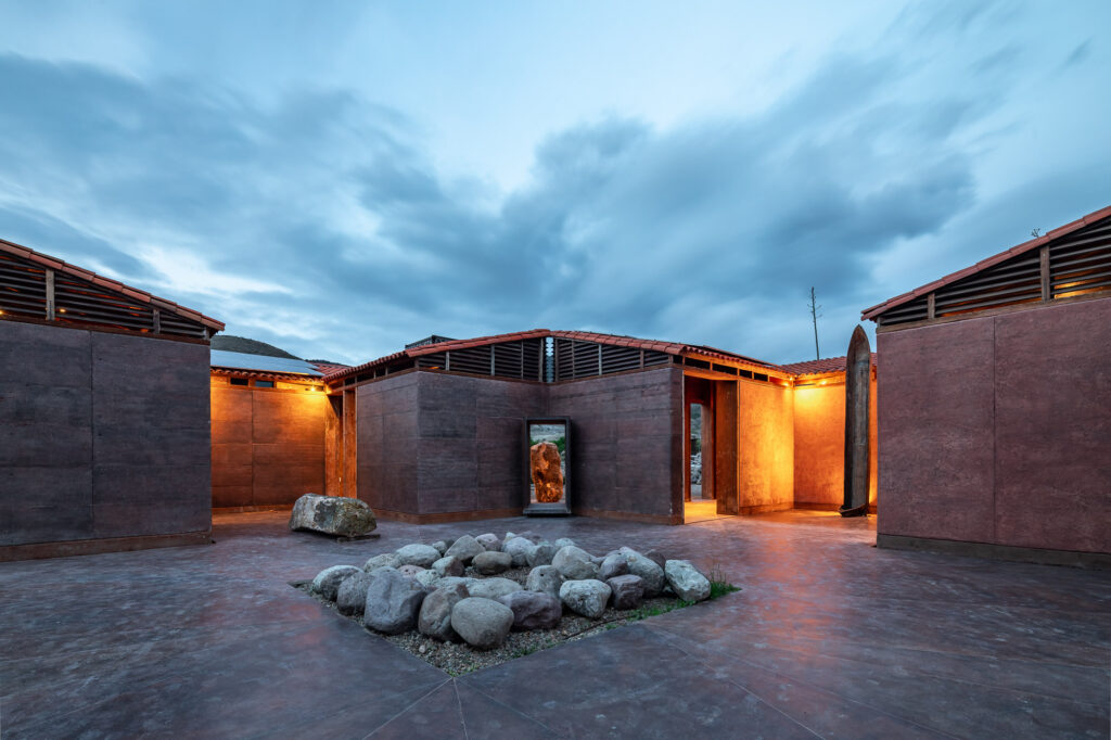 Pátio central da Casa Silencio ao entardecer com paredes de terra e iluminação cênica em arquitetura vernacular.