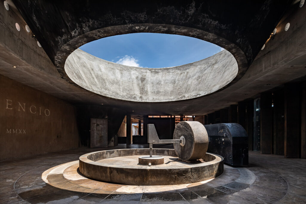 Óculo zenital e tahona tradicional em pedra na Casa Silencio, destacando a arquitetura vernacular mezcaleira.