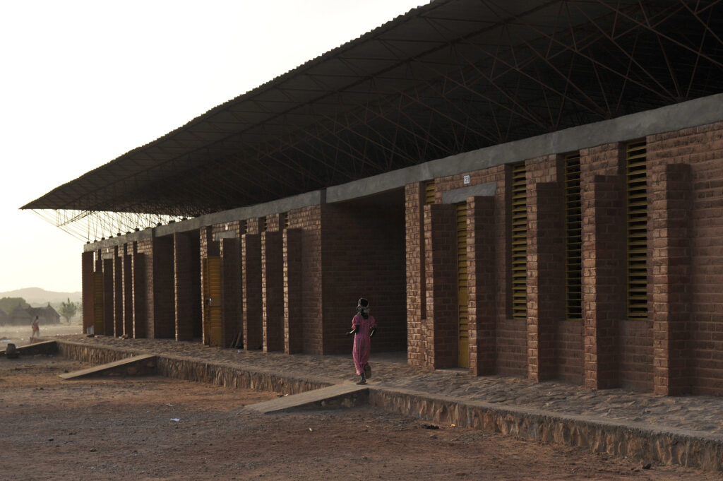 Fachada com brises e tijolos de terra comprimida na Escola Primária em Gando, marco de arquitetura vernacular e conforto térmico.