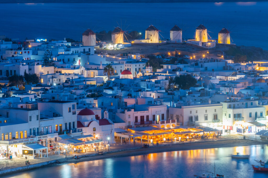 Vista noturna de Chora com arquitetura cicládica iluminada e moinhos, referência de onde ficar em Mykonos.