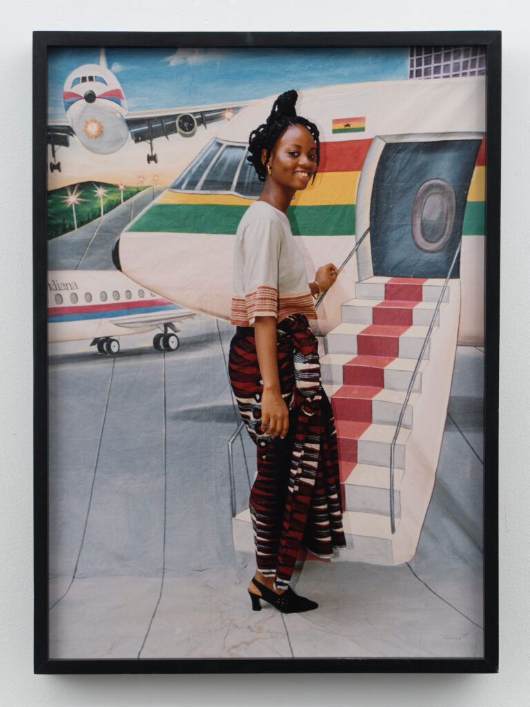 Fotografia Come on Board de Philip Kwame Apagya com mulher diante de cenário pintado de avião na exposição Dreams of This Future.
