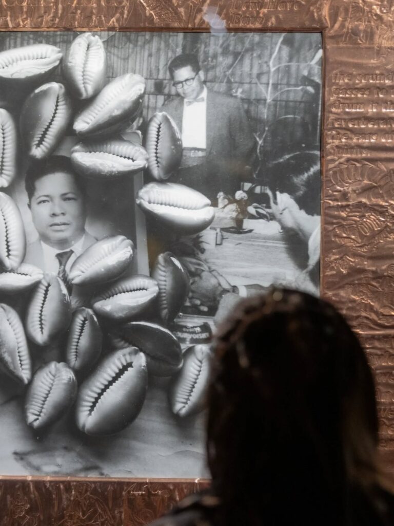 Visitante apreciando obra tátil com búzios e fotos antigas no Sesc São Paulo durante exposição.