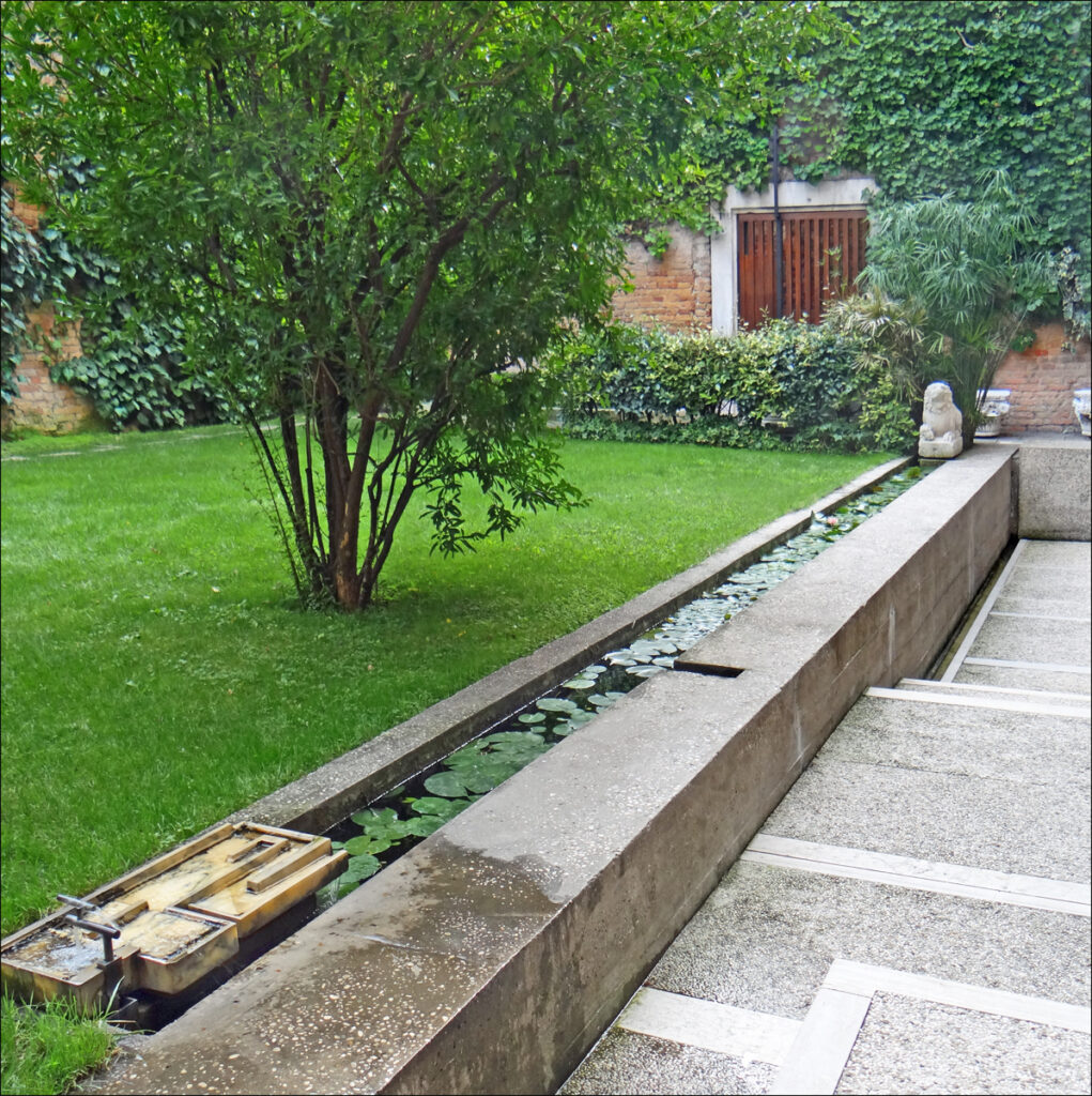 Jardim murado da Fondazione Querini Stampalia com canal linear de água com ninfeias, gramado e muros de tijolos cobertos por hera.