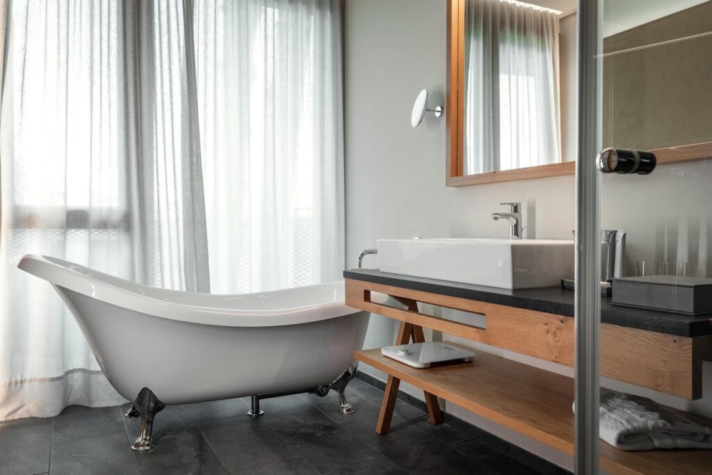 Sala de banho com banheira vitoriana de imersão e bancada em carvalho no Hotel Hubertus, referência entre hotéis de luxo nos Alpes italianos.