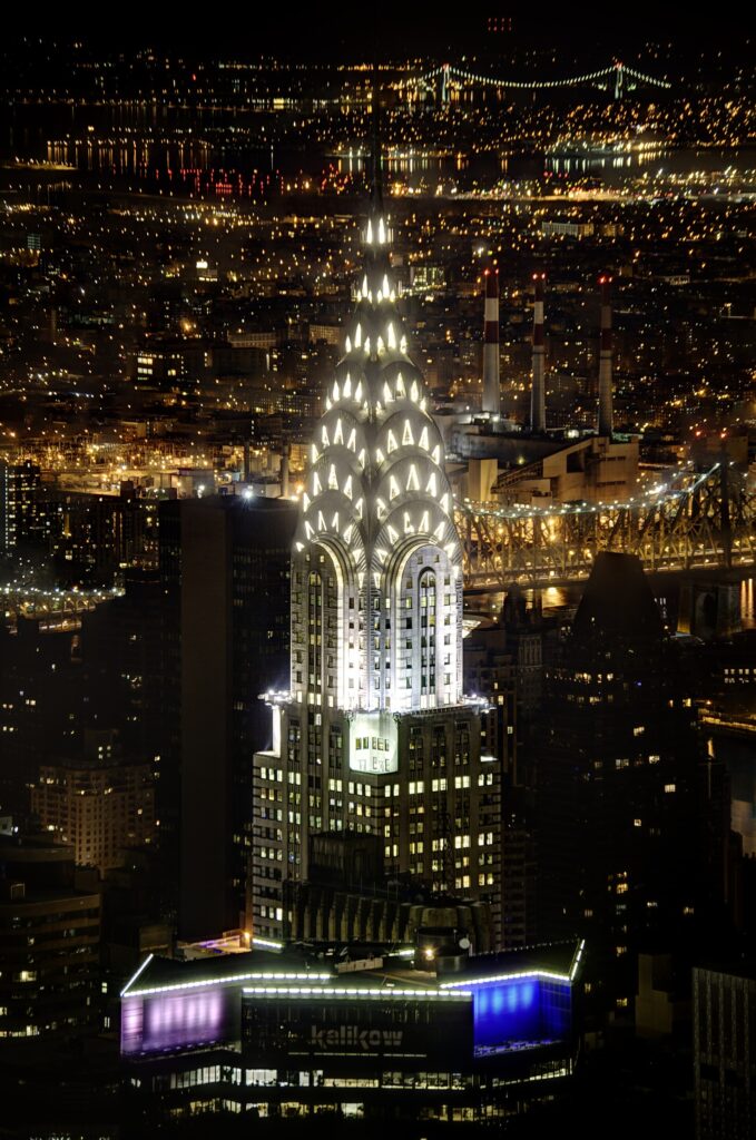 Topo iluminado do Chrysler Building à noite com sua agulha e arcos em aço inoxidável, ícone do Art Déco em Nova York.