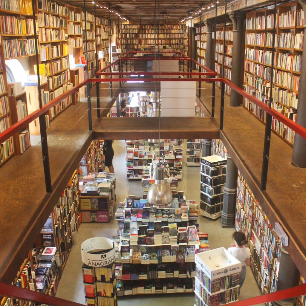 Interior da livraria Más Puro Verso com mezanino, colunas de ferro e estantes de livros em Montevidéu, destaque em roteiro no Uruguai.