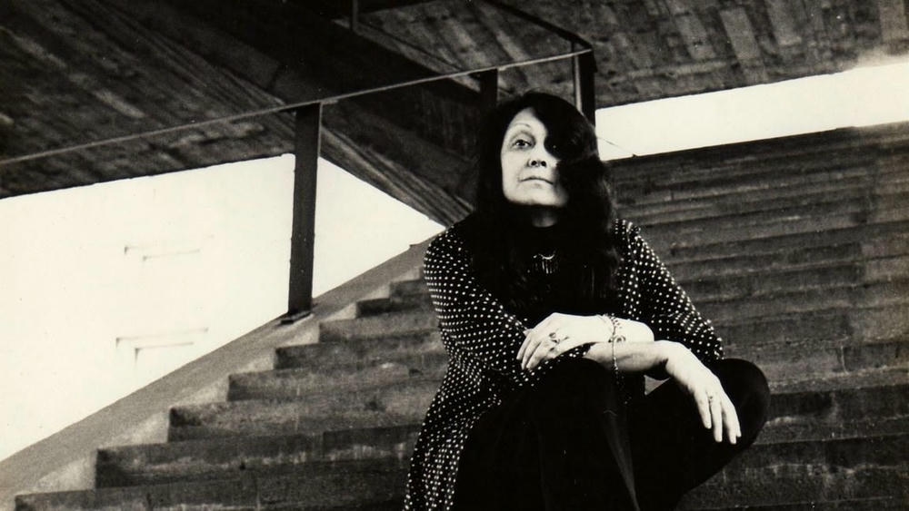 Arquiteta Lina Bo Bardi sentada na escadaria de concreto do MASP, ícone do brutalismo em São Paulo.