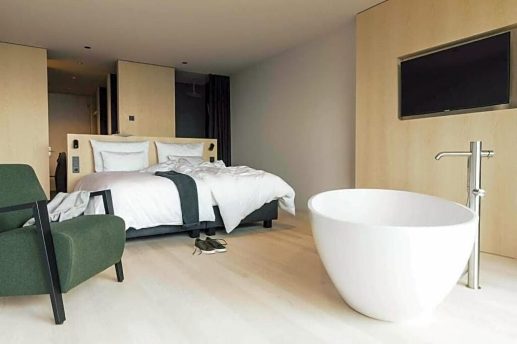Suíte com banheira de imersão e marcenaria clara no Hotel Milla Montis, referência em hotéis de luxo nos Alpes.
