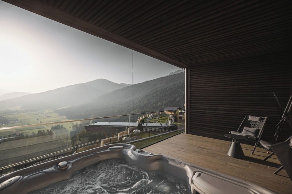 Terraço privativo com jacuzzi e vista panorâmica para as Dolomitas na suíte do Hotel Hubertus, destaque em hotéis de luxo nos Alpes.