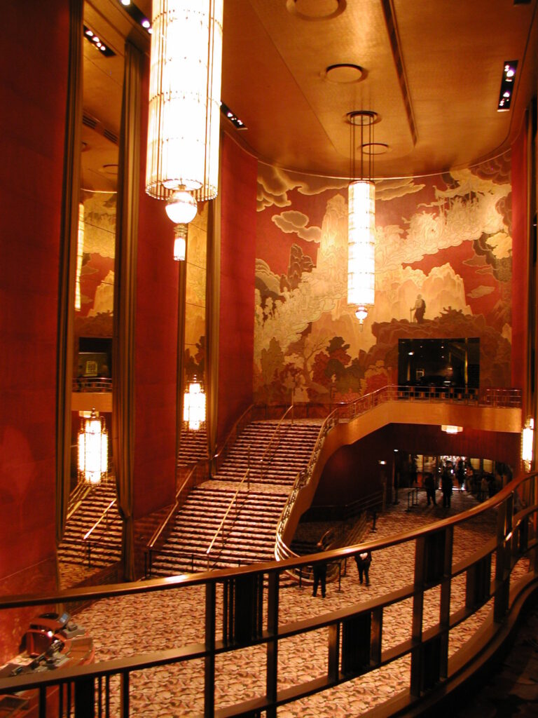 Grand Foyer do Radio City Music Hall com grande escadaria, mural de Ezra Winter e lustres monumentais em estilo art deco.