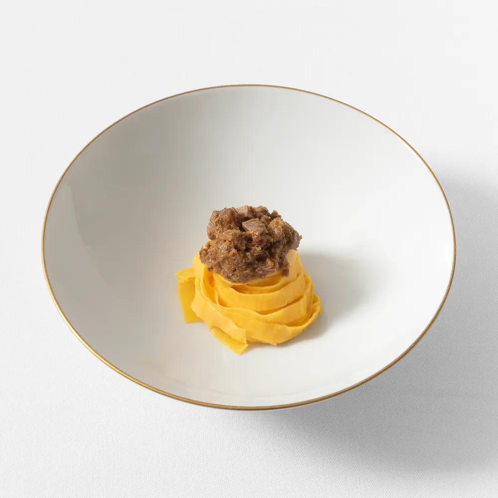Clássico tagliatelle ao ragù da Osteria Francescana servido em bowl de porcelana minimalista branca com borda dourada refinada.