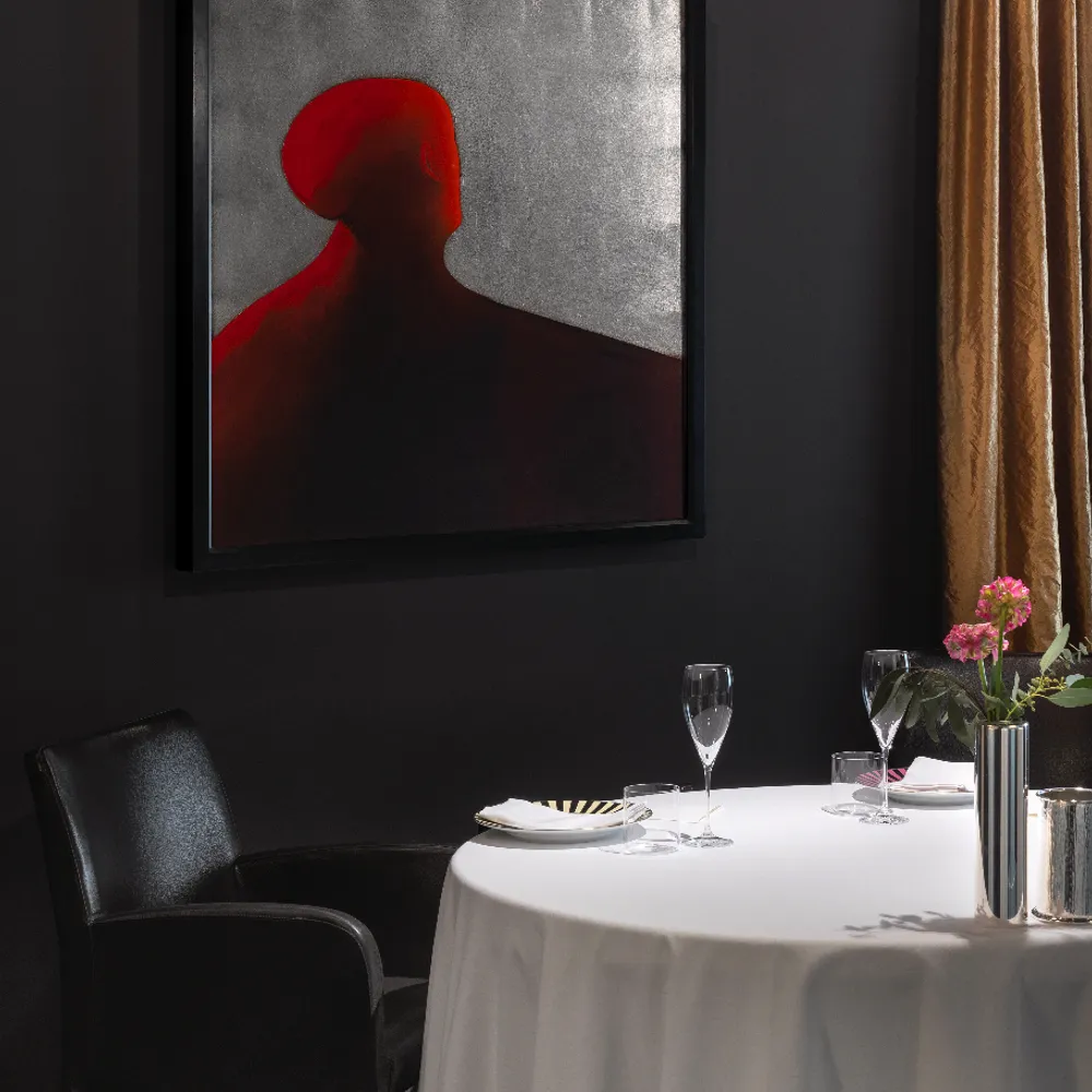 Salão intimista da Osteria Francescana em Modena com mesa iluminada por luz pontual, poltrona de couro e tela de arte contemporânea.