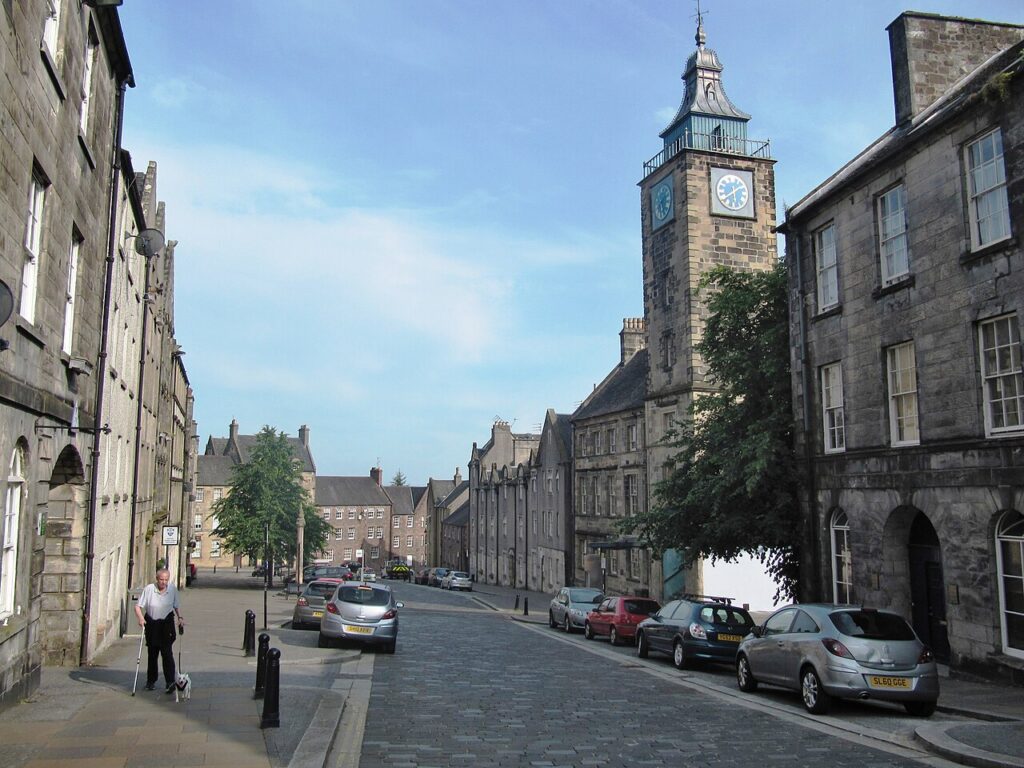 Rua histórica com pavimentação de pedra e a torre do Tolbooth, marco da arquitetura escocesa em Stirling.