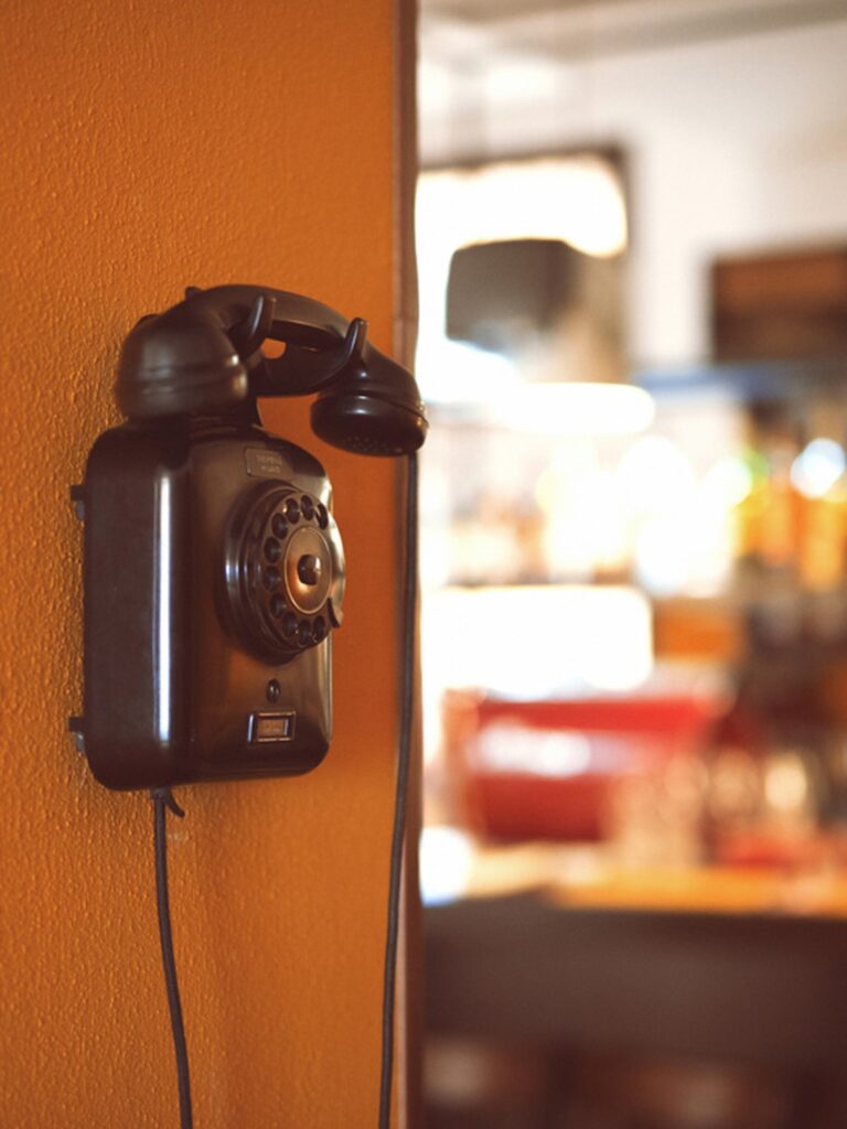 Telefone de baquelite vintage em parede ocre mostarda no restaurante Trippa Milano com iluminação quente ao fundo em Milão.