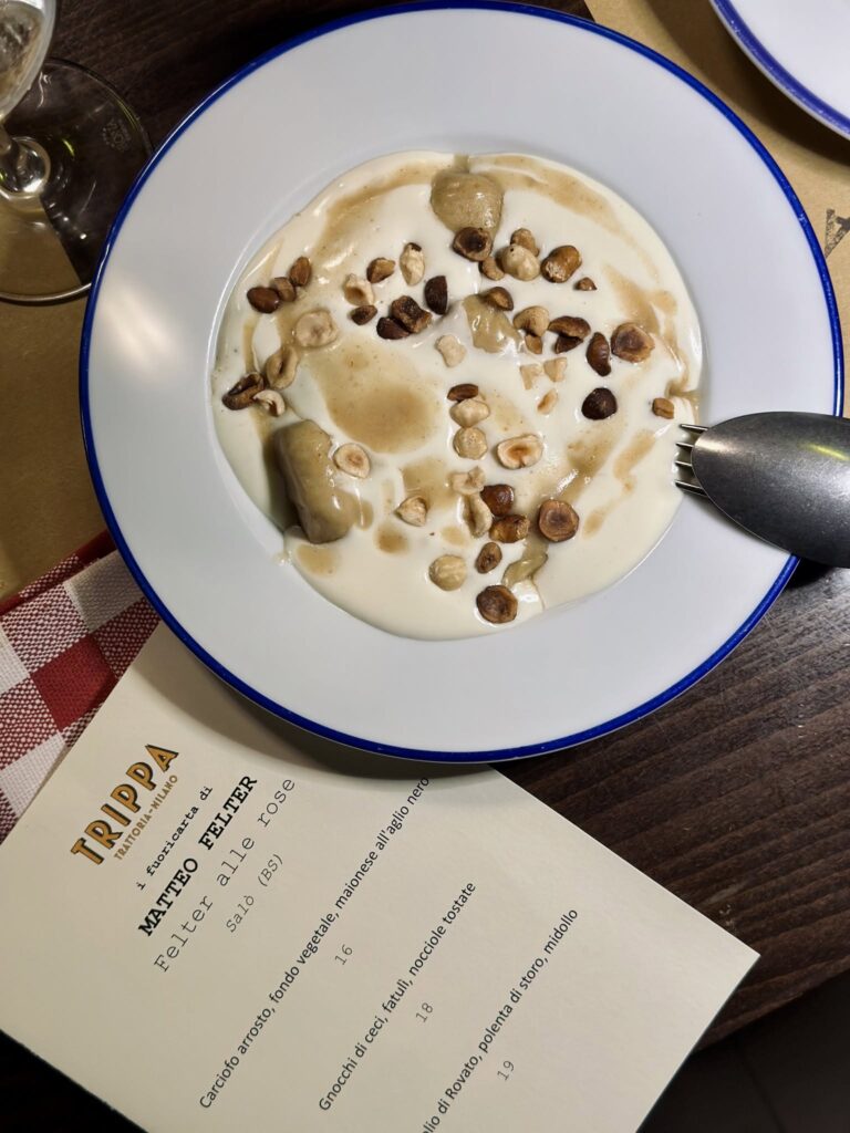 Prato de cerâmica clássica com borda azul e menu vintage sobre mesa de madeira escura no restaurante Trippa Milano.