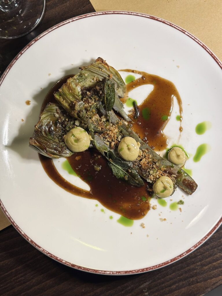 Apresentação gastronômica de alcachofra assada em prato de cerâmica clássico sobre mesa do restaurante Trippa Milano.