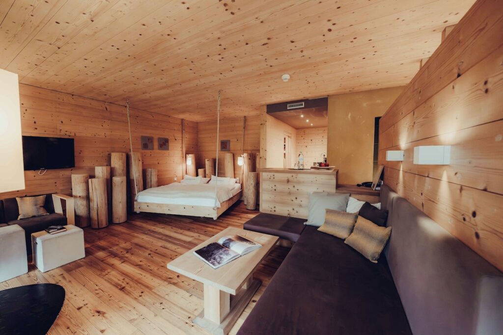 Suíte Secret Forest com cama suspensa e revestimento em madeira no Naturhotel Forsthofgut, referência em hotéis nos Alpes.