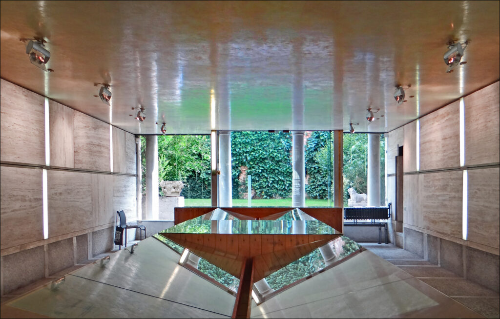 Sala de exposições na Fondazione Querini Stampalia com painéis de travertino, vitrine escultural de vidro e abertura panorâmica para o jardim.
