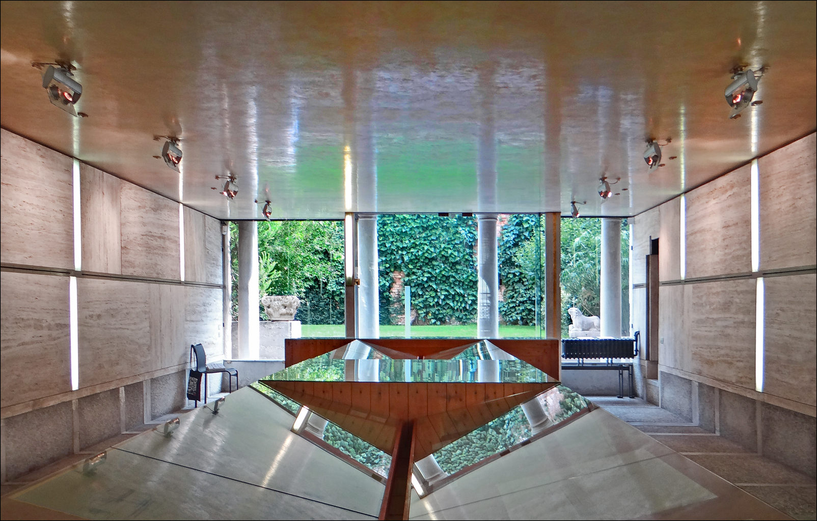 Sala de exposições na Fondazione Querini Stampalia com painéis de travertino, vitrine escultural de vidro e abertura panorâmica para o jardim.