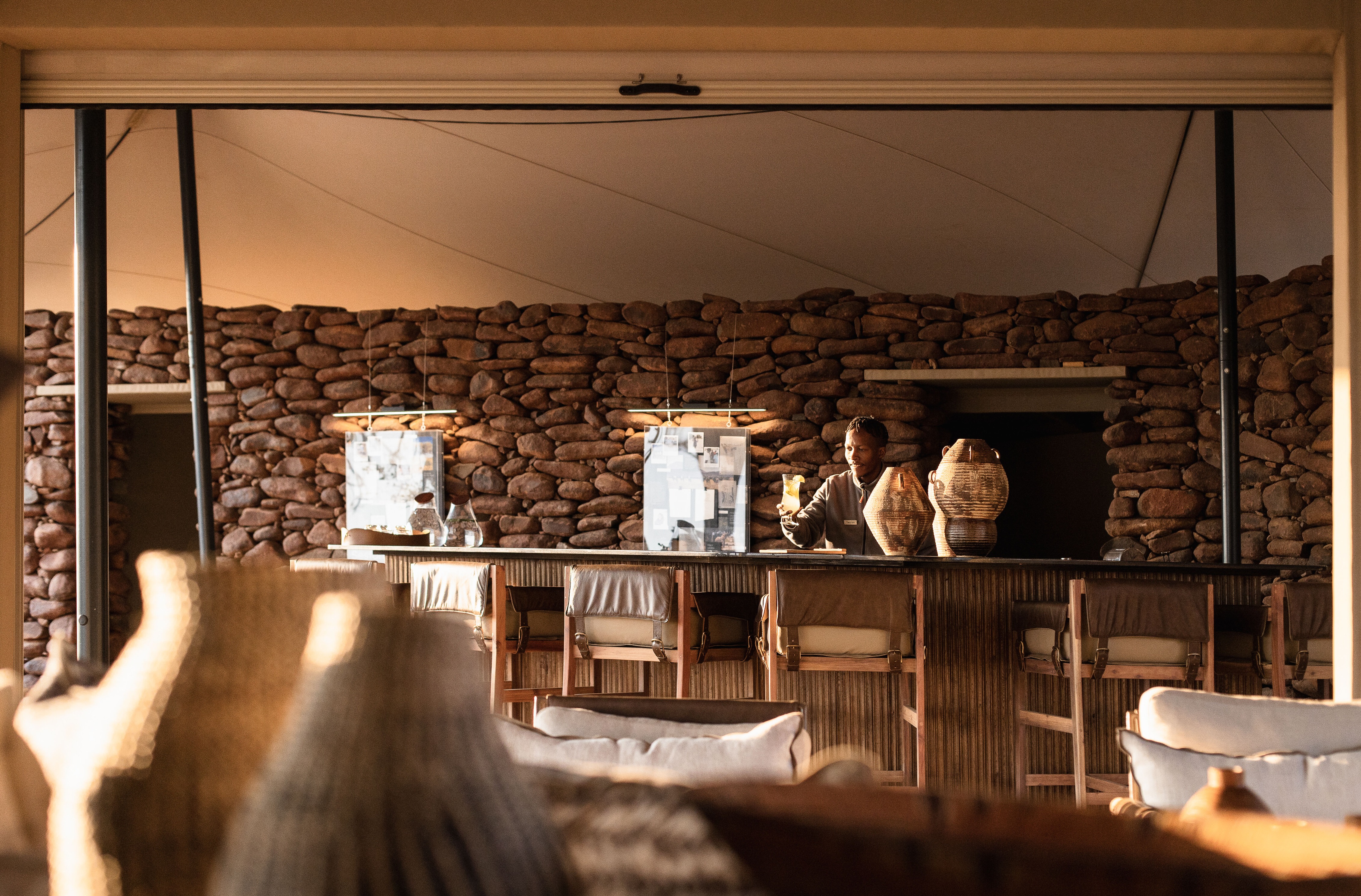 Bar com balcão de madeira ripada e parede de pedra no Desert Rhino Camp.