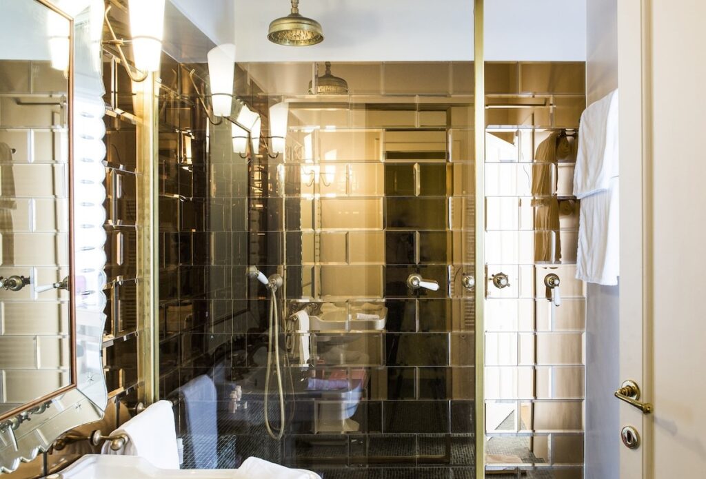 Banheiro sofisticado do hotel boutique G-Rough Roma com revestimento de espelho bisotado âmbar e metais em latão.