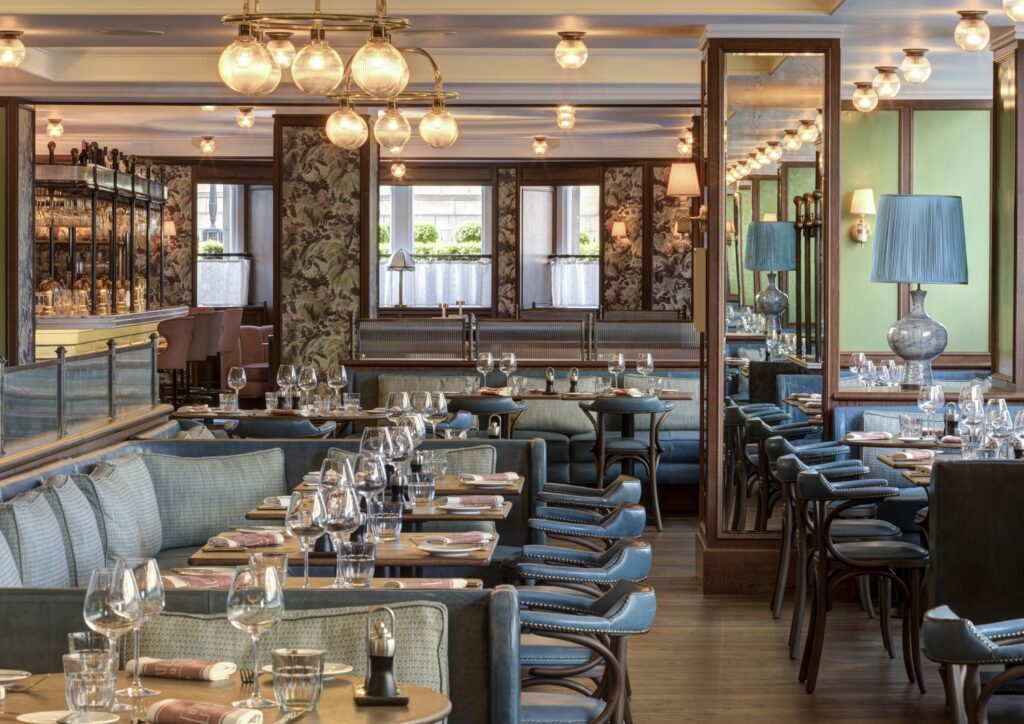Salão de refeições da Brasserie Prince no Balmoral hotel com bancos estofados em couro azul, divisórias de vidro canelado e pilares espelhados.