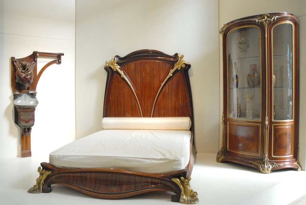 Quarto Art Nouveau no Musée d'Orsay com cama monumental em madeira nobre torneada, detalhes em bronze dourado e cristaleira curva.