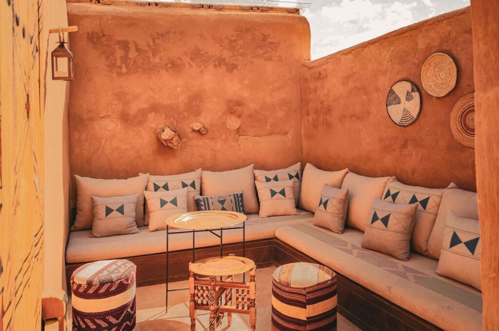 Lounge externo com sofás de alvenaria e cestarias artesanais na parede do Dar Tantora.