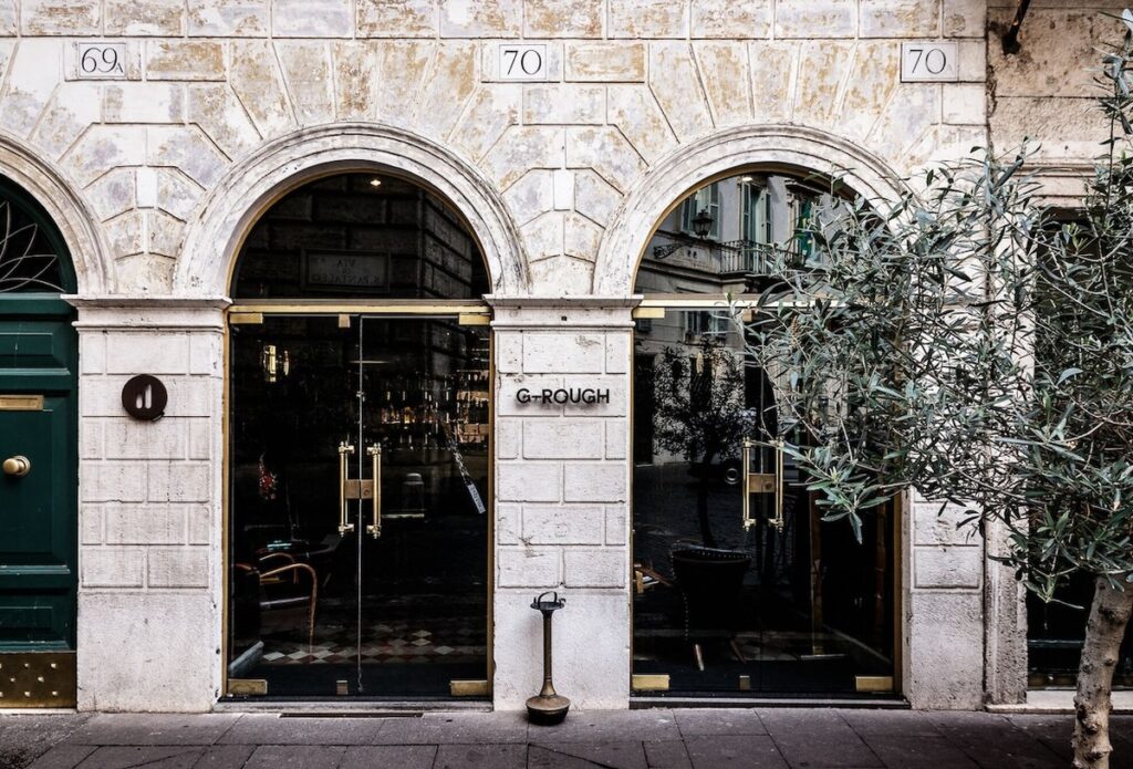 Fachada histórica em travertino com arcos e portas de latão dourado do hotel boutique G-Rough Roma.