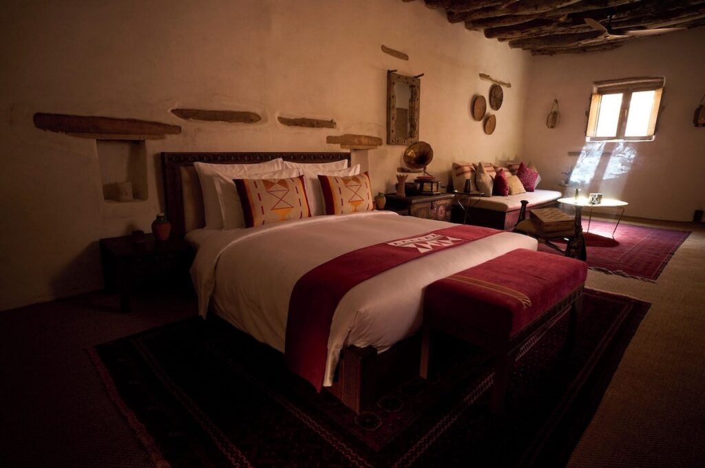 Quarto de casal com cabeceira de madeira entalhada e toques bordô no Dar Tantora.